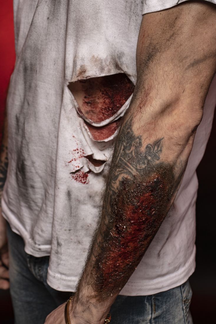 Close detail of a silicone road-rash wound on a forearm with blood spatter on the shirt